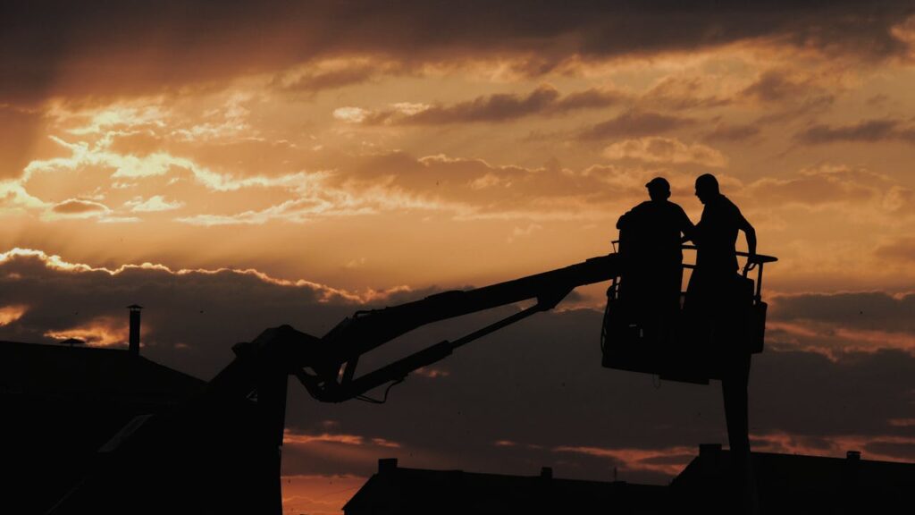 Silhouette of two workers on a crane against a dramatic sunset sky.